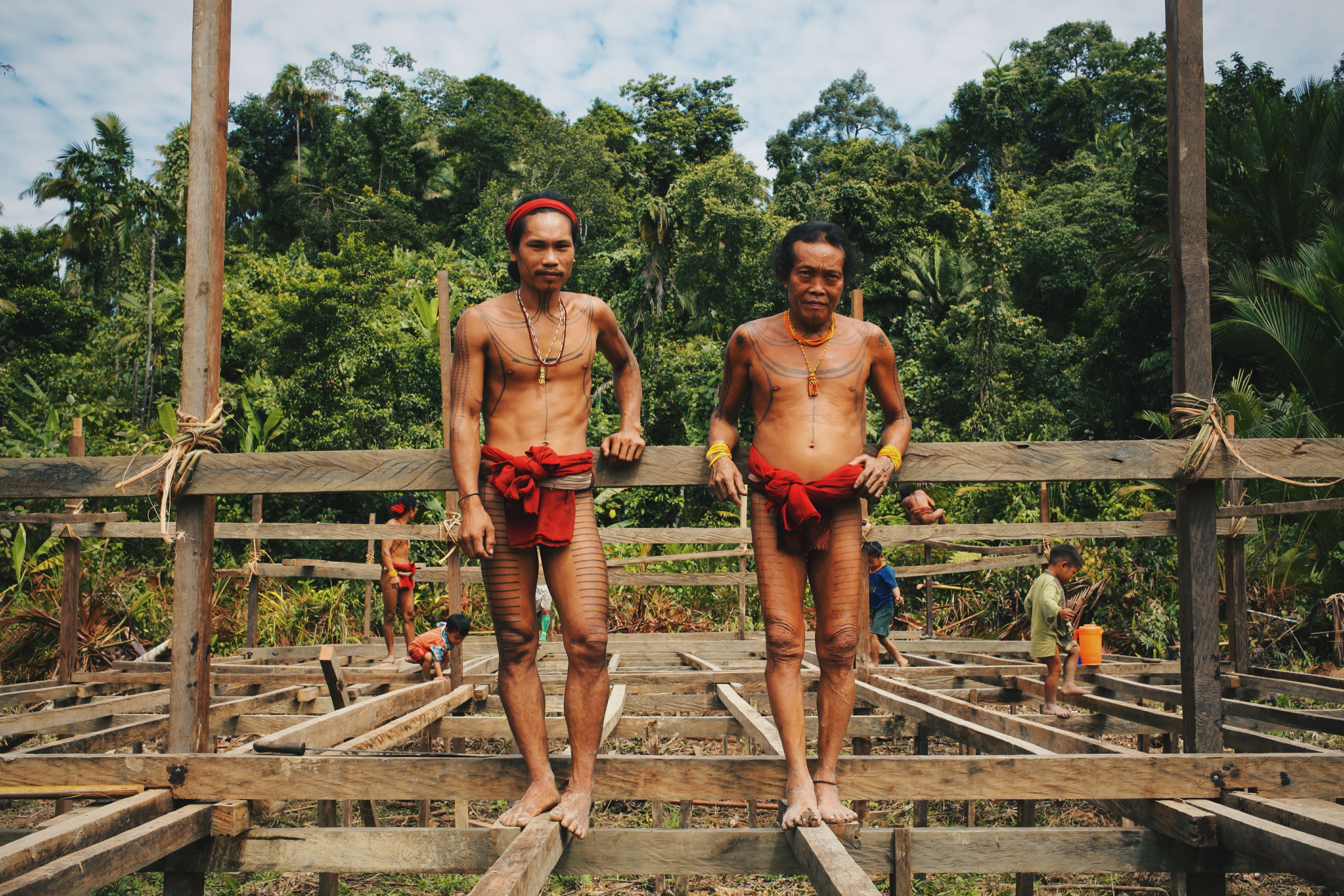 Two Mentawai men standing on a wooden platform in the jungle